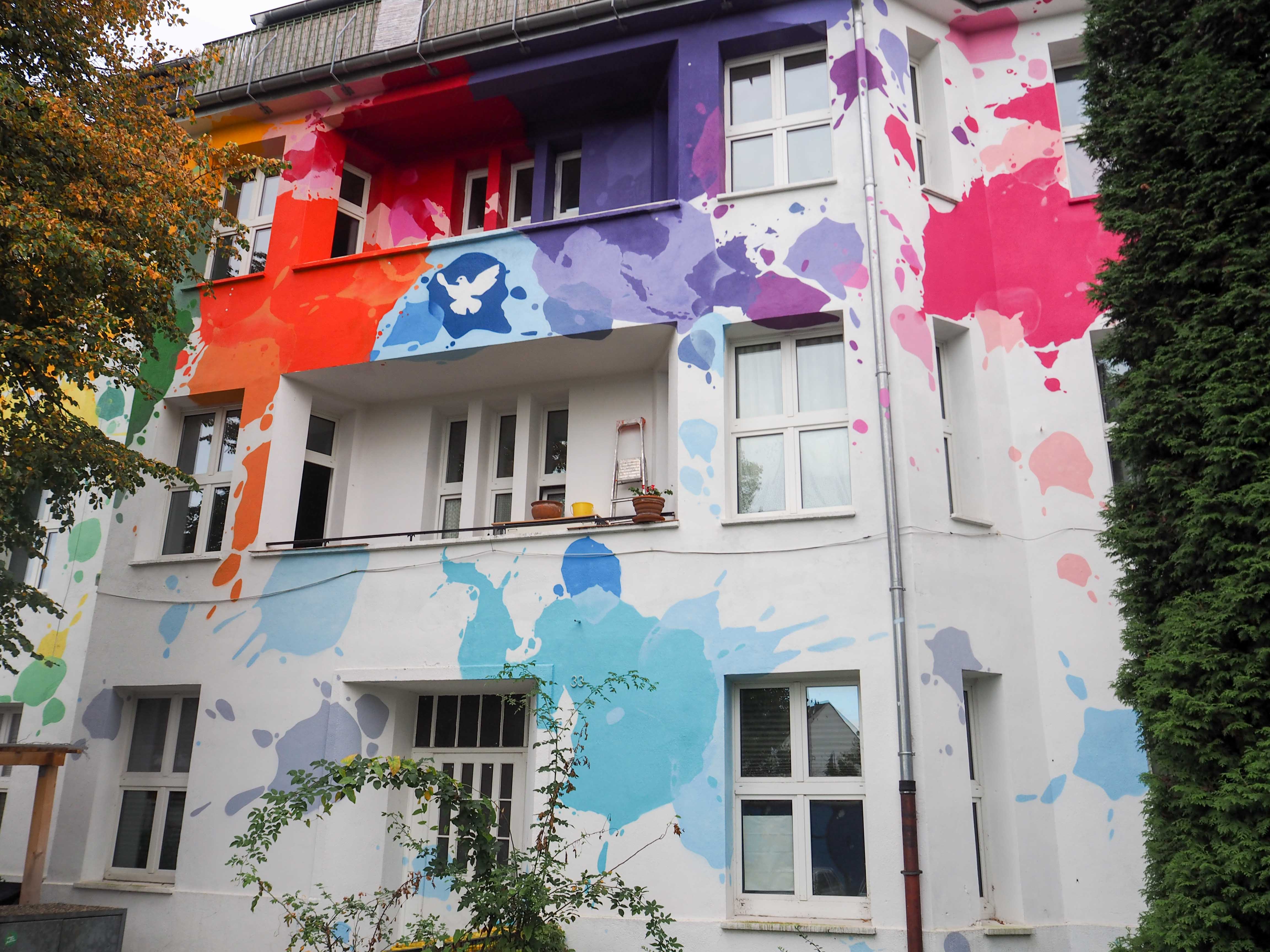 unbekannte Künstler haben bunte Farbklekse und eine Friedenstaube auf die Hauswand gemalt