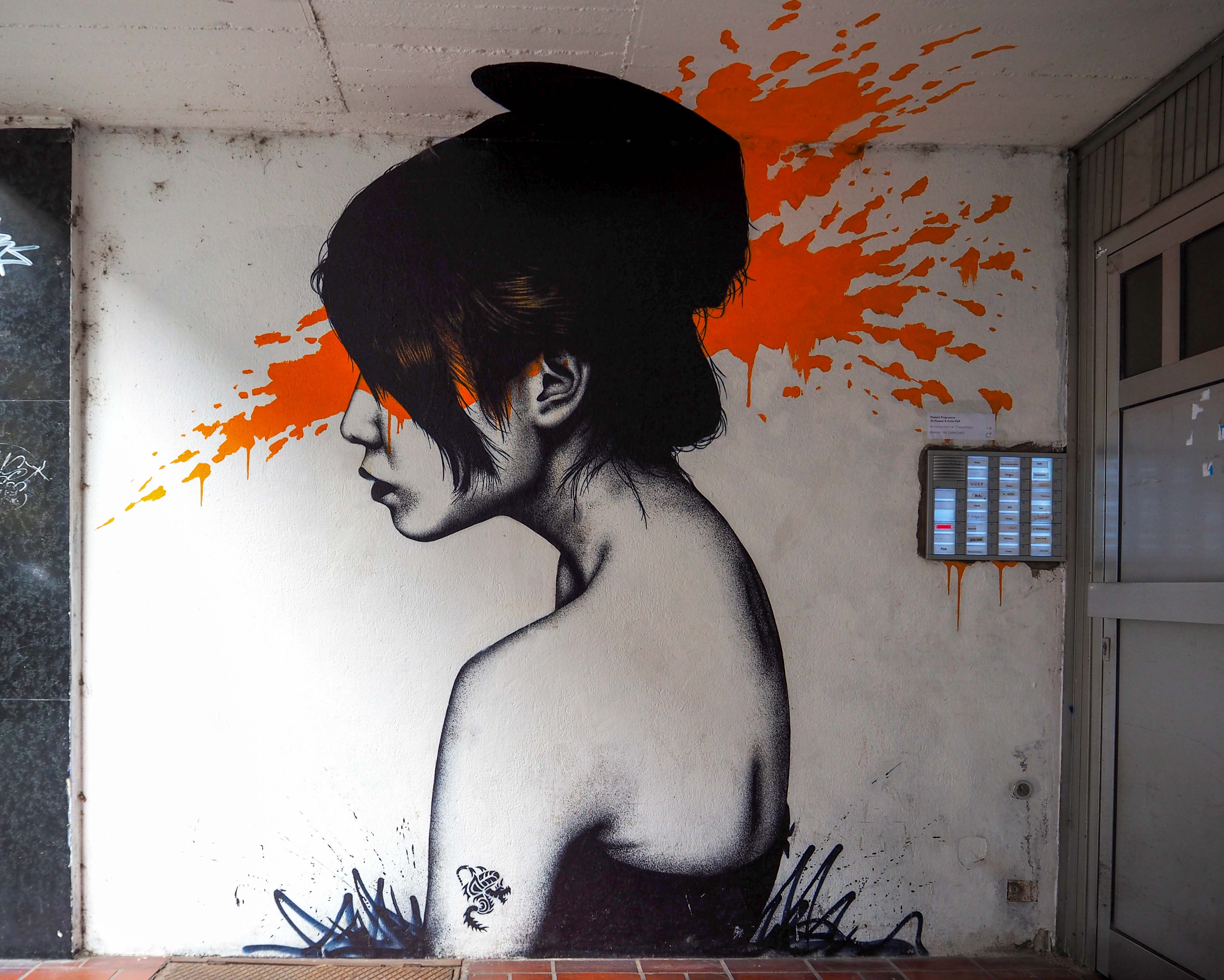 FinDac malte sein Moonchild, eine asiatisch wirkende junge Frau mit orangem Farbhintergrund in einem Hauseingang