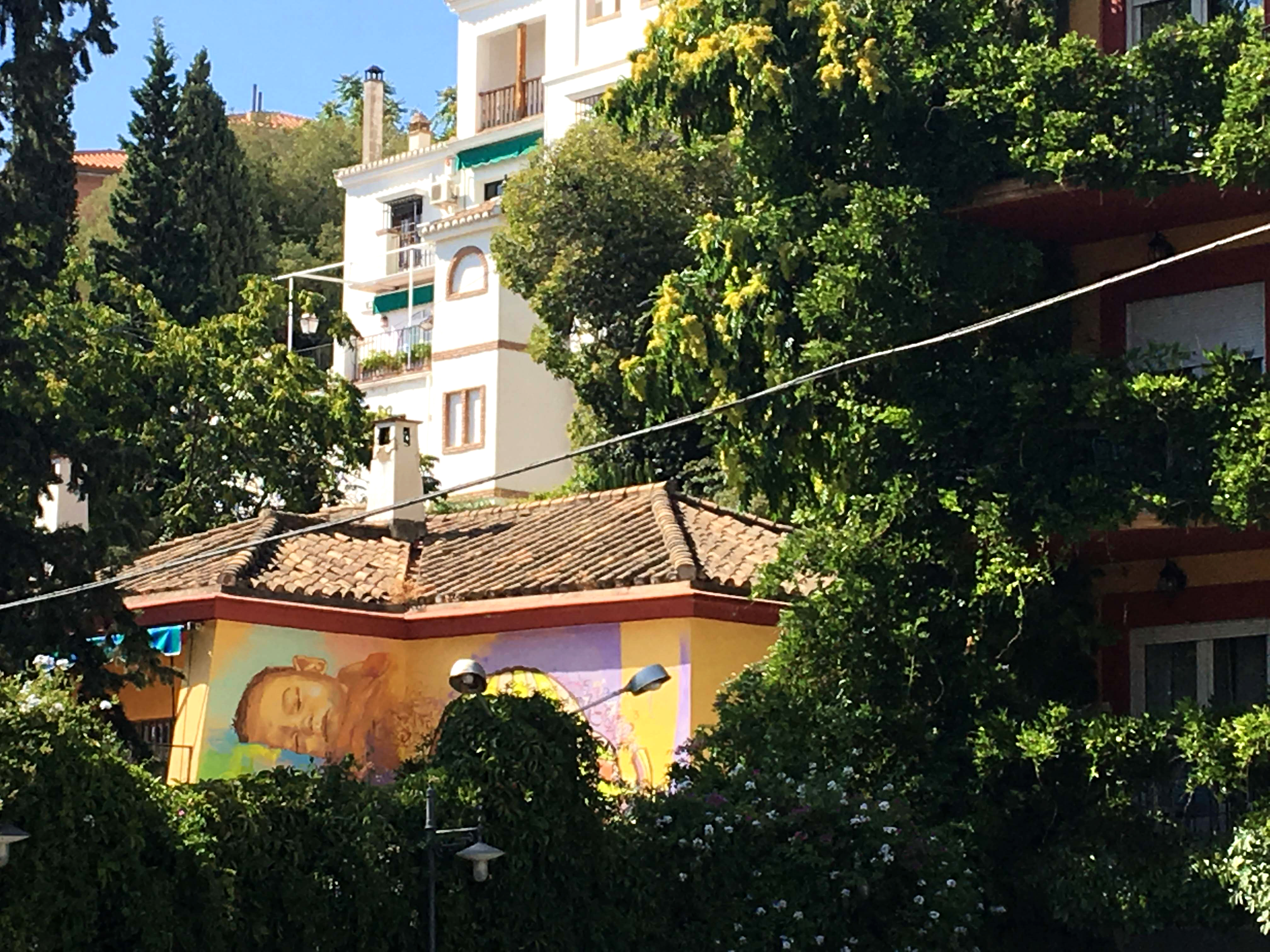 Die Wand eines Kindergartens an der sich hinter viel Grün ein Mural von El Niño de las Pinturas versteckt