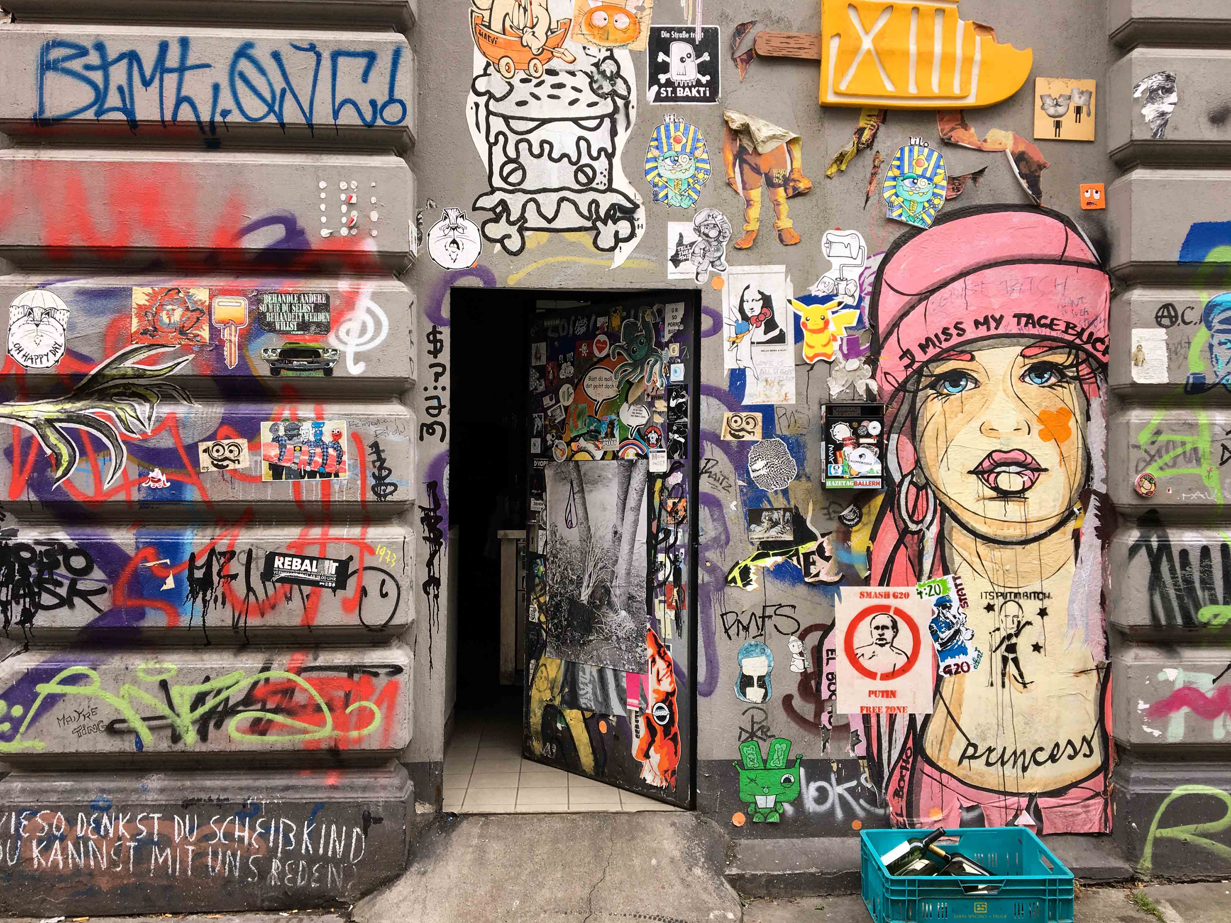 eine Hauswand mit geöffneter Tür die mit Stencils, Graffiti und Paste ups übersät ist. an der Seite prangt ein überlebensgroßer Frauenkopf von El Bocho