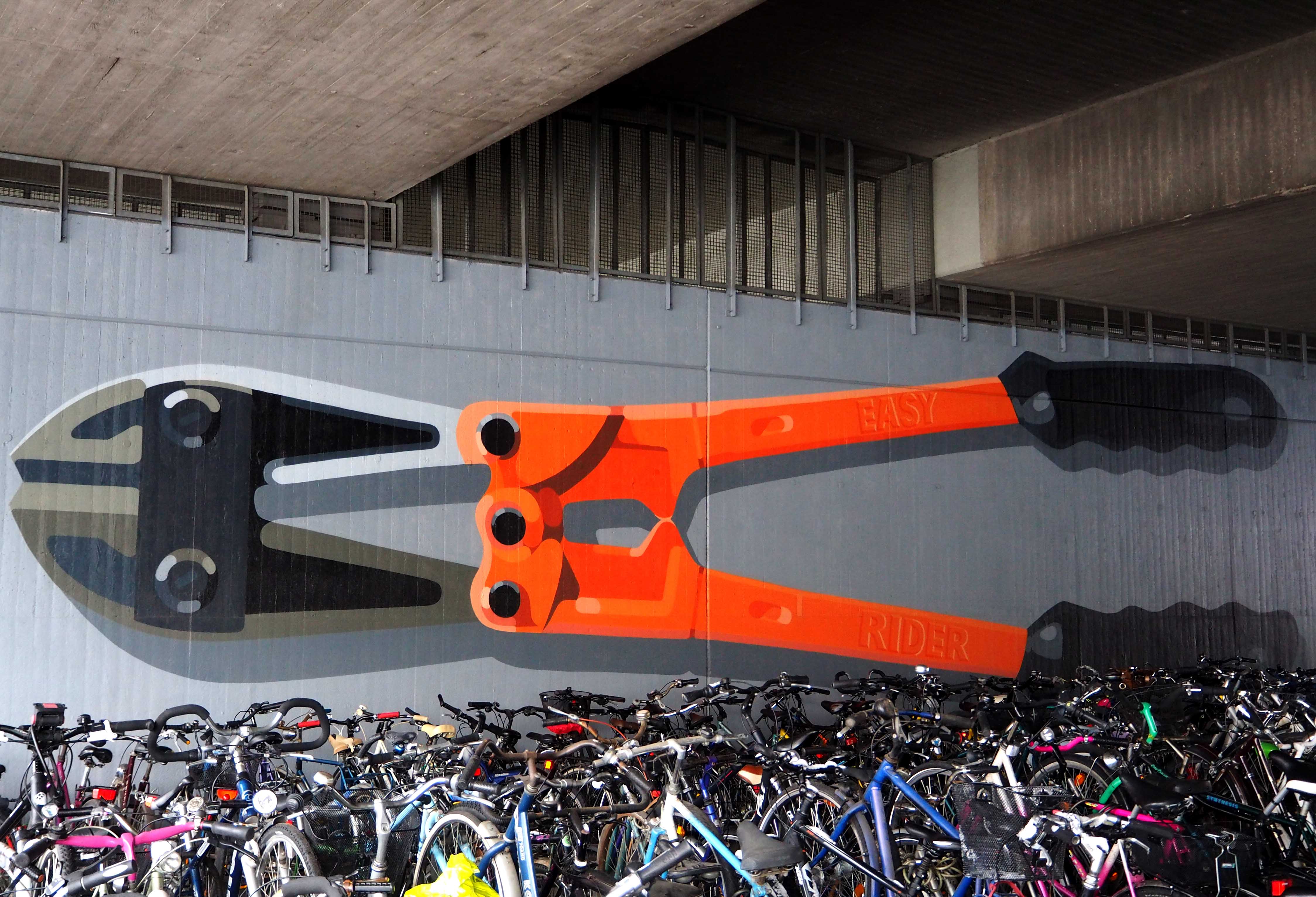 unter einer Brücke, ein Mural dass vor sehr vielen Fahrrädern einen Bolzenschneider zeigt