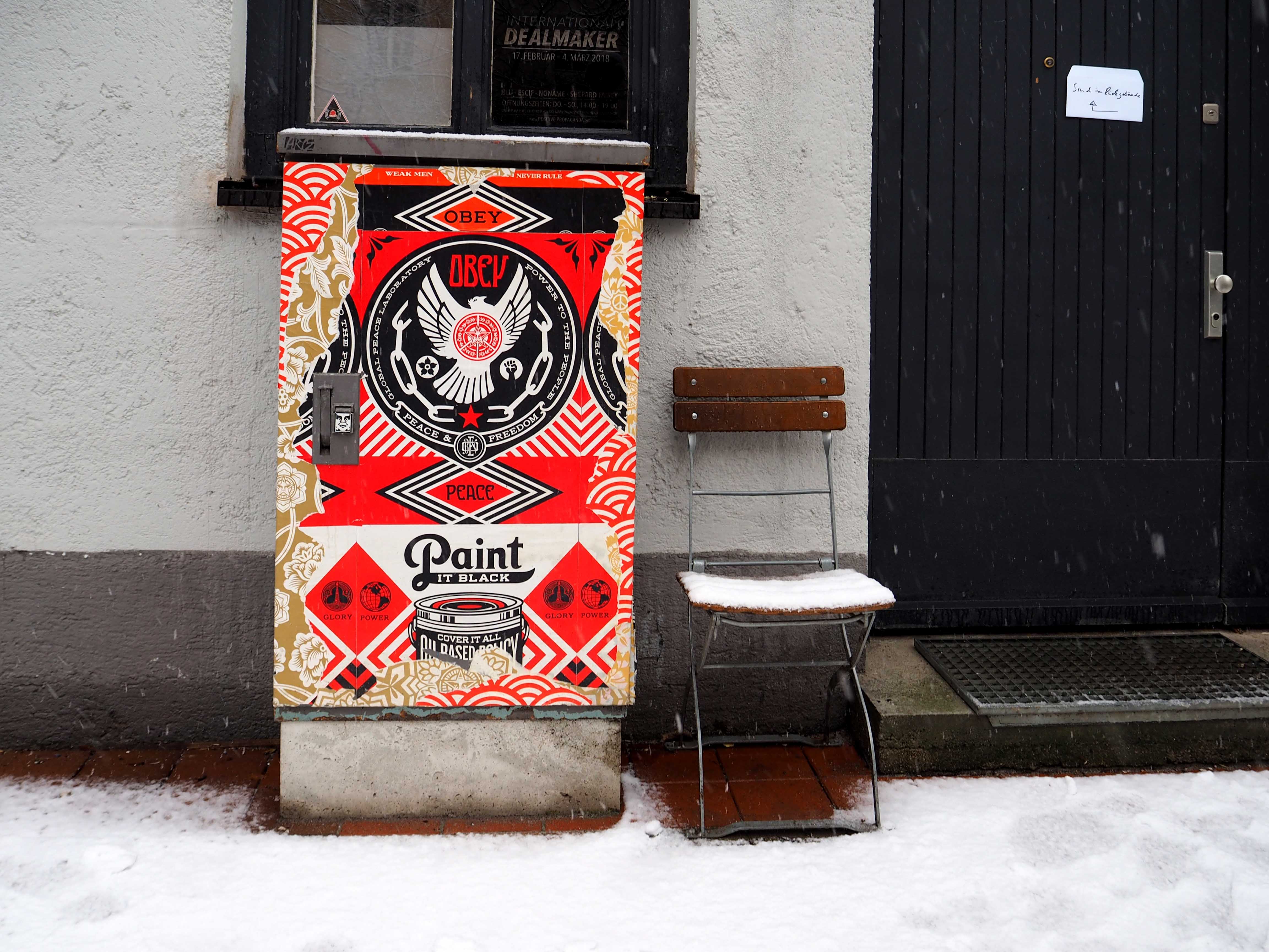 vor einem Eingang steht ein Stromkasten, der von Shepard Fairey gestaltet ist