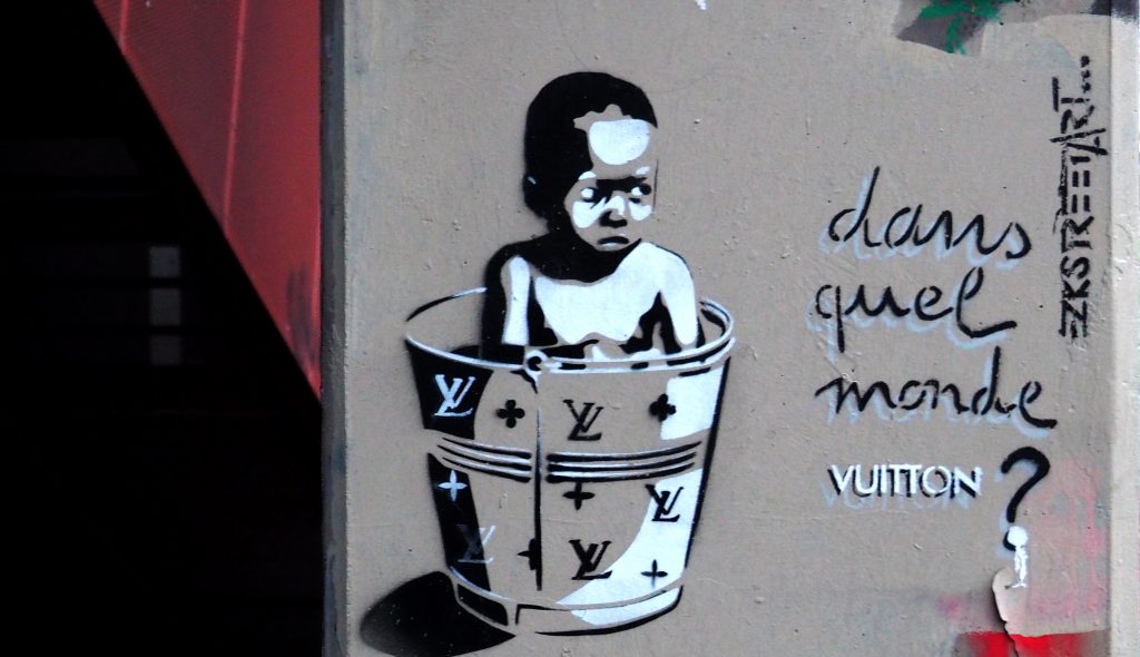 "In welcher Welt" Stencil von EZK, zeigt einen Jungen in einem Louis Vuitton Eimer