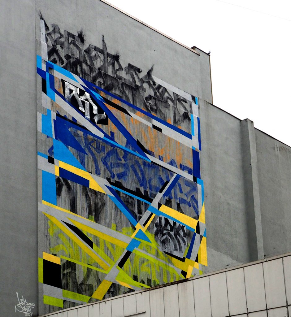 Sowat und Lek haben gelb/blau/schwarze geometrische Muster an die Wand gemalt.