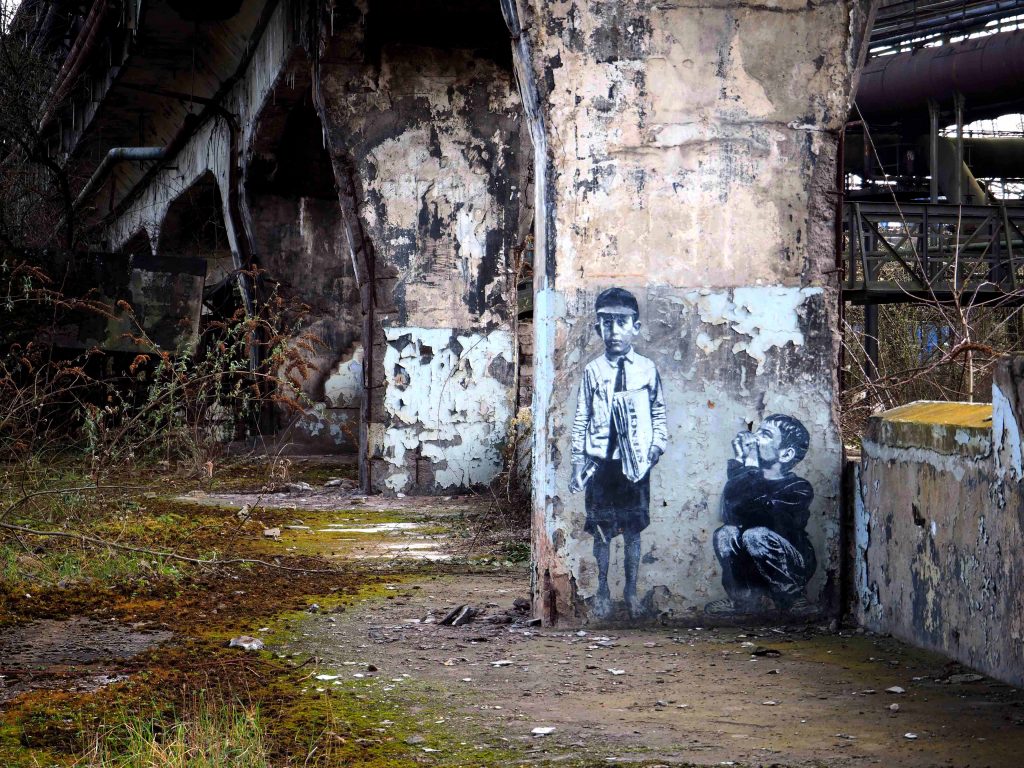 Zwei Jungen hocken auf der Arbeit von Jef Aérosol auf dem Pfeiler einer Brücke.